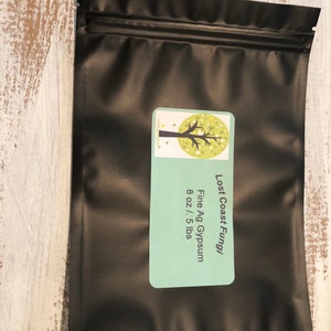 May include: Black resealable bag with a white label that says "Lost Coast Fungi Fine Ag Gypsum 8 oz / 5 lbs" and a green tree illustration.
