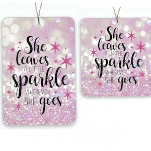 May include: Two pink and white glitter car air fresheners with the text "She leaves a little sparkle wherever she goes" in black lettering.
