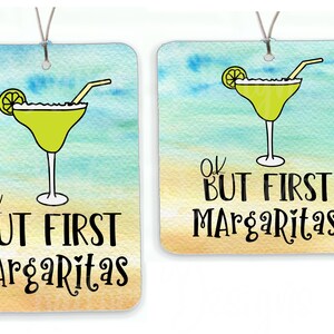 May include: Two car air fresheners with a beach background and a margarita glass with a lime and straw. The text on the air fresheners reads "Ok but first margaritas".