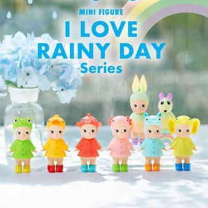 May include: A selection of Sonny Angel mini figures from the "I Love Rainy Day" series. Each figure is dressed in a colourful raincoat and wellington boots, with animal-themed hats. A rainbow and text are in the background.