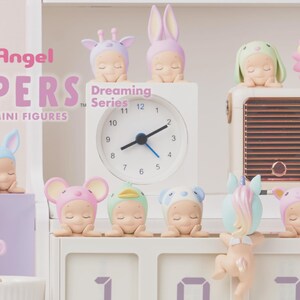 Op de afbeelding: Een collectie van decoratieve Sonny Angel Hippers Dreaming Series mini-figuren met diverse personages in dierenthema hoofddeksels. De figuren staan opgesteld naast een witte analoge klok en een radio in vintage-stijl op een witte plank.