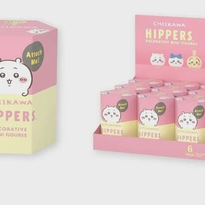 May include: Pink and yellow boxes and display featuring "Chikawa Hippers" decorative mini figures. The boxes and display have a cartoon character on them. The display has several cylindrical boxes with the same character. The text "Attach Me!" is on the boxes.