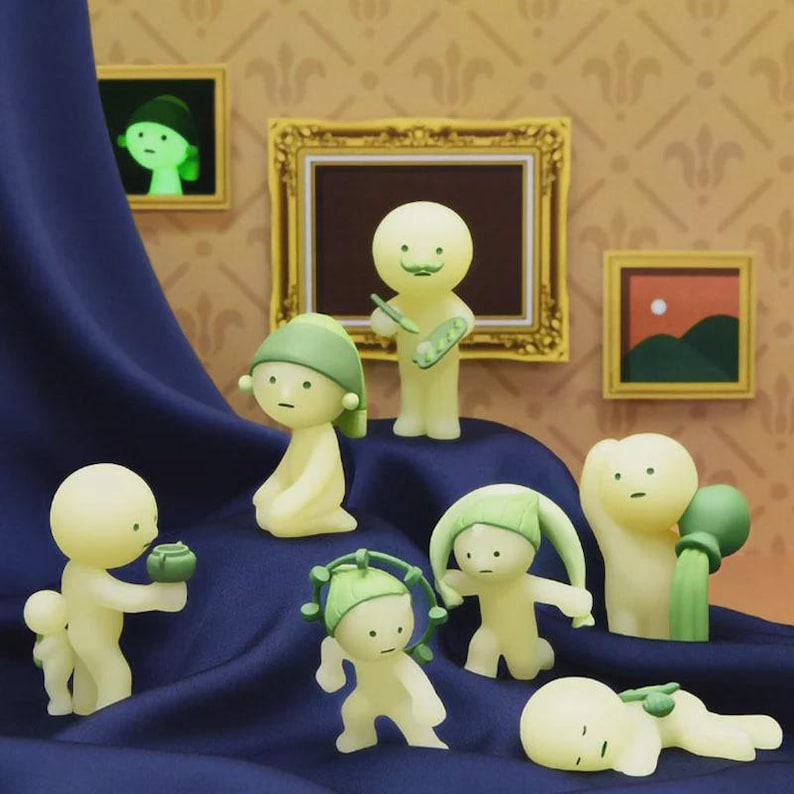 May include: A group of glowing figurines in different poses, some wearing green hats. One figure holds a paintbrush and palette, while others interact with small objects. The background features framed art and a dark blue draped fabric.