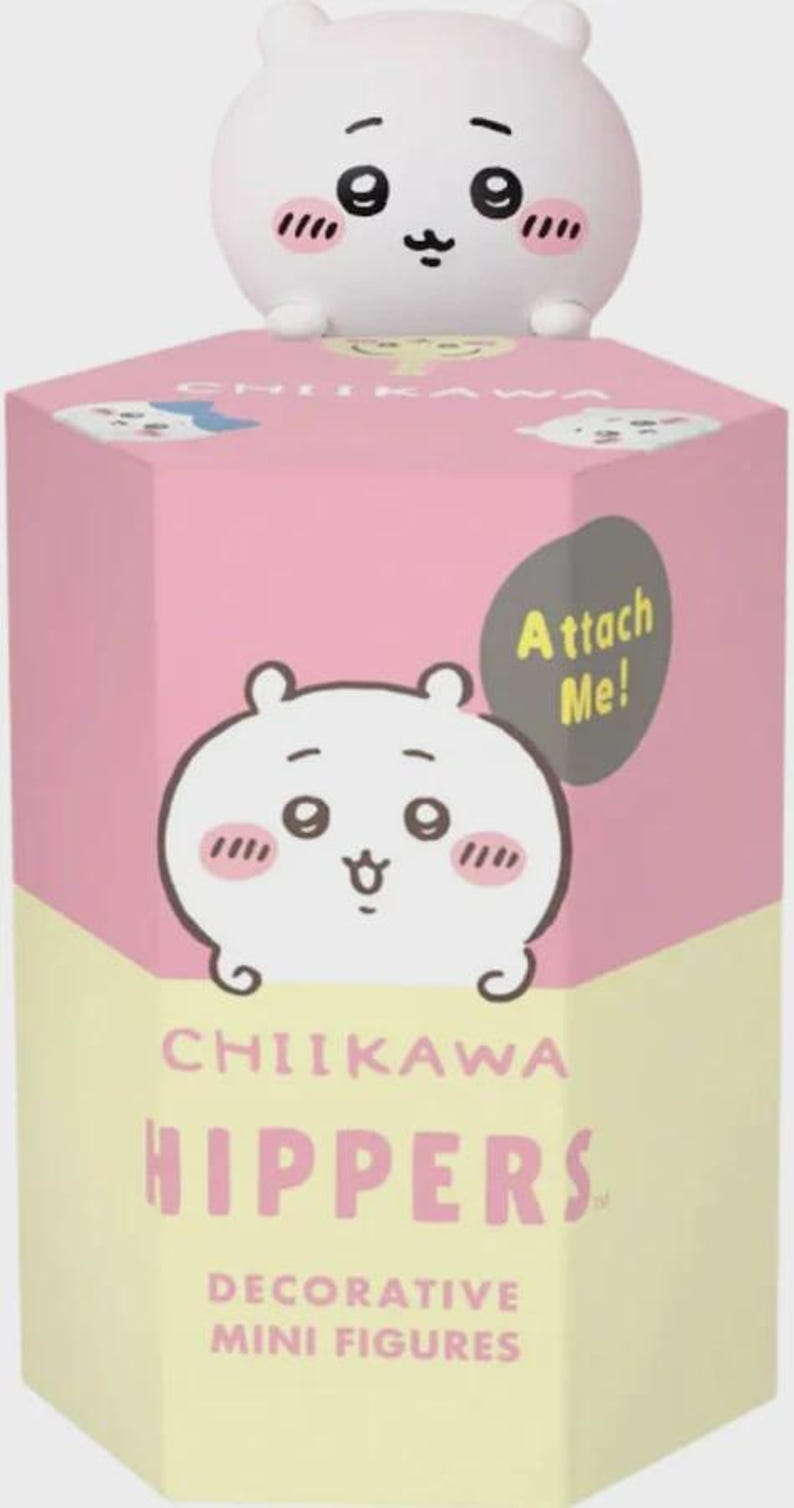 May include: A white Chiikawa figure sits atop a pink and yellow box. The box features a cartoon illustration of the character with the text "CHIIKAWA HIPPERS DECORATIVE MINI FIGURES". A gray speech bubble says "Attach Me!"