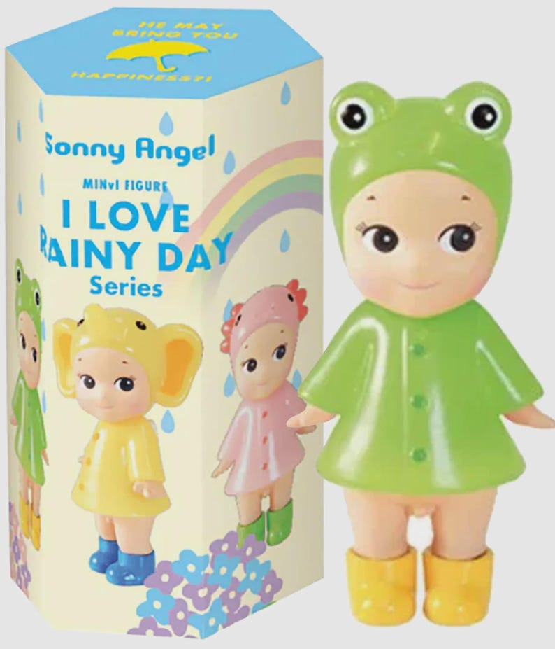 May include: A Sonny Angel mini figure from the I Love Rainy Day Series, depicting a doll in a green frog hat, raincoat, and yellow wellington boots. The box displays other figures and the text "I Love Rainy Day Series".