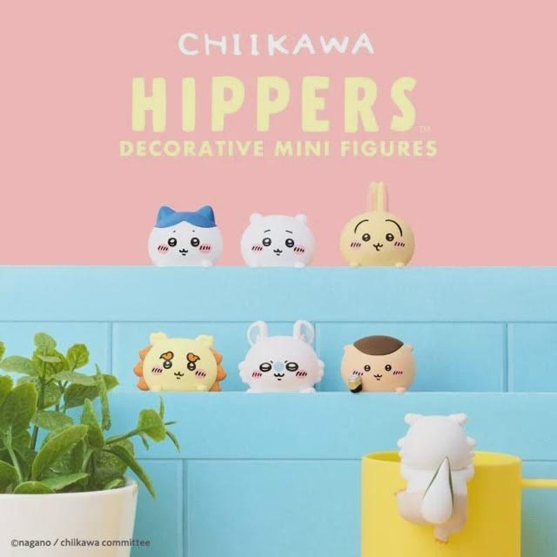 May include: A collection of decorative mini figures, featuring various cute characters with expressive faces. The figures are in pastel colors, including white, yellow, and blue. The text "CHIIKAWA HIPPERS" is displayed at the top.