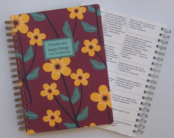 May include: A spiral-bound notebook with a dark maroon cover featuring yellow flowers and green leaves. A teal rectangular label on the cover reads, Flowers are happy things. - P.G. Wodehouse. The inner page displays various printed quotes about happiness.