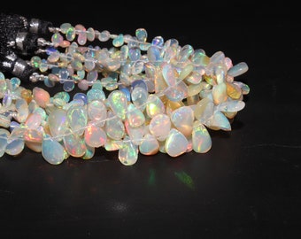 May include: A strand of iridescent white opal gemstone beads in a teardrop shape. The beads are strung on a clear thread and have a natural, irregular shape.