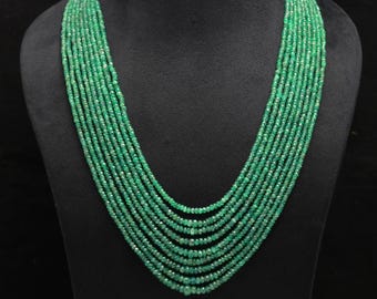 Könnte beinhalten: Eine mehrsträngige Halskette aus kleinen, facettierten Smaragdperlen. Die Halskette ist in einem kaskadierenden Design angeordnet und zeigt die leuchtend grüne Farbe der Edelsteine. Die Halskette wird auf einer schwarzen Schaufensterpuppe präsentiert.