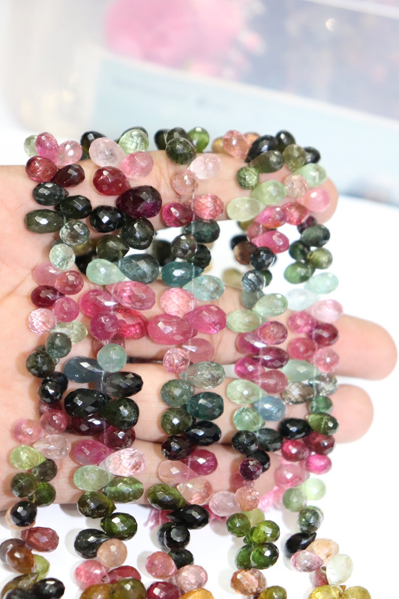 Puede incluir: Una hebra de cuentas de piedras preciosas facetadas multicolores. Las cuentas son en tonos de rosa, verde, negro y azul. Las cuentas son de forma ovalada y tienen un acabado facetado.