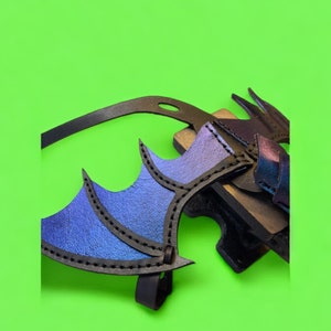 May include: A black leather dragon wing costume piece with blue and purple iridescent accents. The wing is attached to a black leather strap.