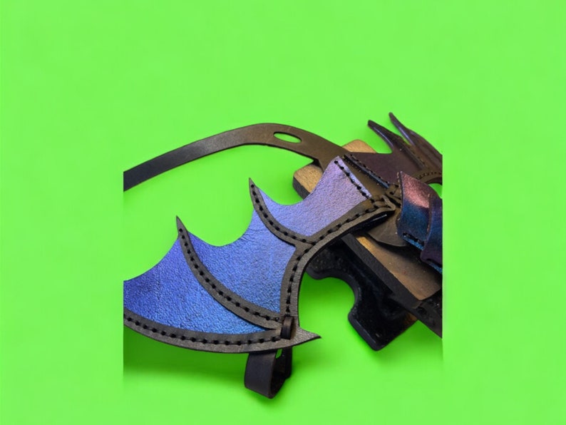 May include: A black leather dragon wing costume piece with blue and purple iridescent accents. The wing is attached to a black leather strap.