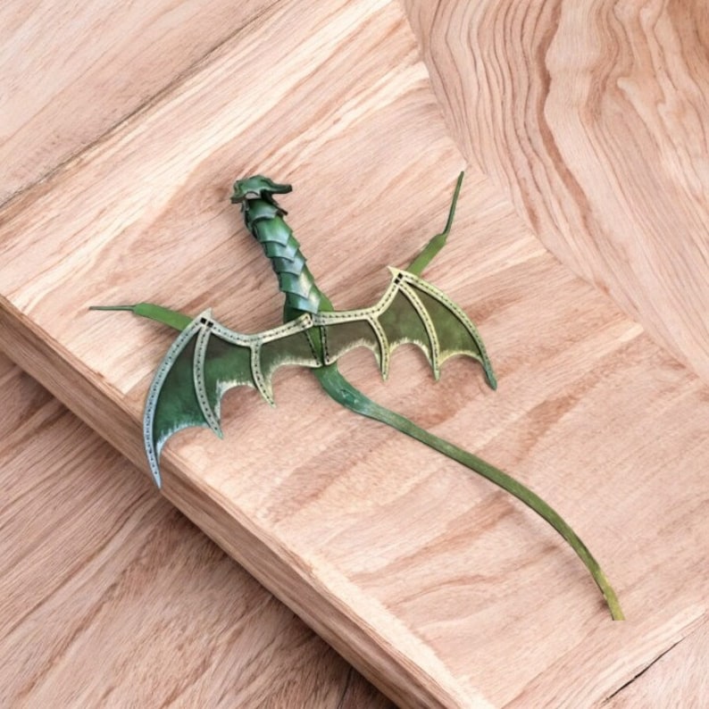 May include: A green leather dragon with wings outstretched, crafted in a detailed style. The dragon is posed on a wooden surface.