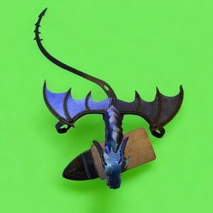 May include: A blue and black dragon costume with wings and a tail. The dragon is holding a wooden sword in its mouth.