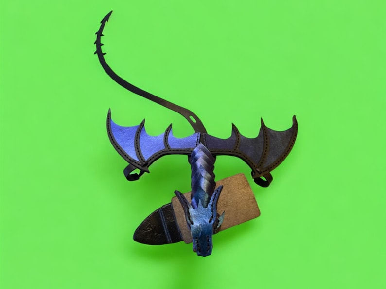 May include: A blue and black dragon costume with wings and a tail. The dragon is holding a wooden sword in its mouth.