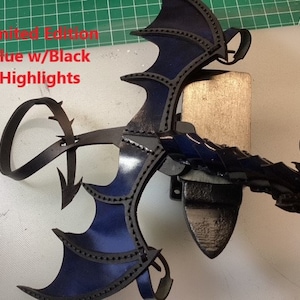 May include: A blue leather dragon wing with black highlights. The wing is attached to a black leather strap. The strap has a loop at the end. The text "Limited Edition Blue w/Black Highlights" is visible in the image.