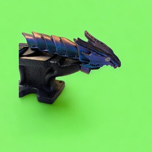 May include: A black metal anvil with a blue and purple dragon sculpture on top. The dragon has a textured, scaly design.