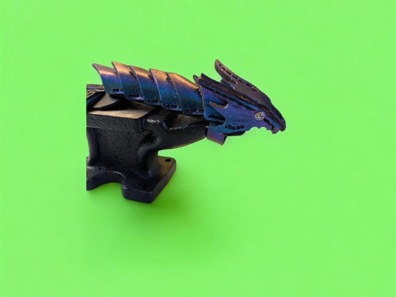 May include: A black metal anvil with a blue and purple dragon sculpture on top. The dragon has a textured, scaly design.