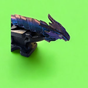 May include: A black metal vise with a purple and blue dragon sculpture attached to it. The dragon is made of layered metal and has a detailed design.