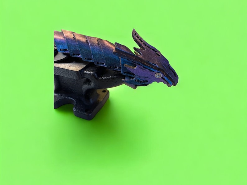 May include: A black metal vise with a purple and blue dragon sculpture attached to it. The dragon is made of layered metal and has a detailed design.