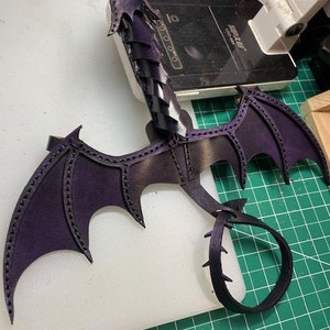 May include: A purple leather dragon tail with black wings and a pearlescent purple finish. The tail is curled into a circle and the wings are spread out. The dragon is a limited edition piece.