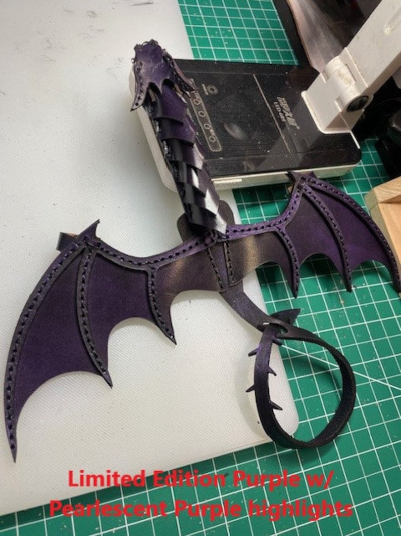 May include: A purple leather dragon tail with black wings and a pearlescent purple finish. The tail is curled into a circle and the wings are spread out. The dragon is a limited edition piece.