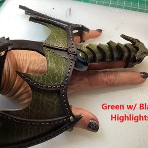 May include: Green leather dragon claw ring with black highlights. The ring is worn on a finger and has a wrist cuff.