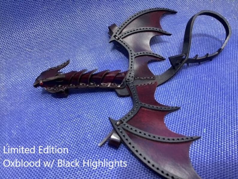 May include: Limited Edition Oxblood leather dragon wings with black highlights. The wings are attached to a leather strap.