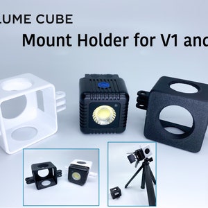 May include: White, black and grey plastic mount holders for a Lume Cube V1 and V2 light. The holders have a GoPro mount on the side. The text "Lume Cube Mount Holder for V1 and V2" is at the top of the image. The text "Made in USA" is at the bottom of the image.