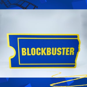 May include: A blue and yellow 3D printed replica of a Blockbuster Video ticket. The ticket has a yellow border and the word "BLOCKBUSTER" printed in yellow letters.
