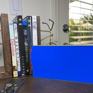 May include: A blue and yellow blank ticket stub with rounded corners. The ticket stub is sitting on a wooden surface in front of a bookshelf with several Blu-ray discs.
