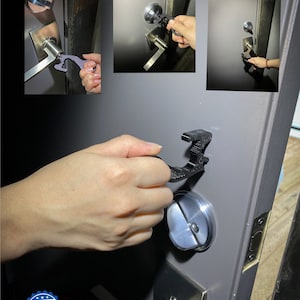 May include: A black plastic tool with multiple functions, including a door opener, a stylus, and a phone stand. The tool is being used to open a door handle. The tool has the words "Made in USA" printed on it.
