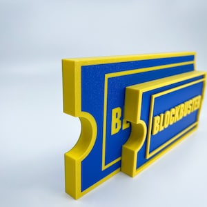 May include: A blue and yellow 3D printed sign that reads "BLOCKBUSTER".