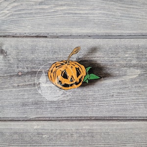 May include: A wooden Halloween decoration featuring an orange jack-o'-lantern with a carved face, a brown stem, and green leaves. The pumpkin is set against a gray wooden background, perfect for seasonal decor.