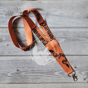 May include: Orange lanyard with a black snake design and the text "Cartoon Hooligans" printed on it. The lanyard has a metal clasp.