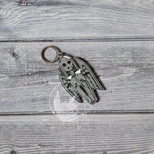 Può includere: Un portachiavi argentato con una figura grigia di Angelo Piangente. L'angelo ha le ali e una lunga veste fluida.