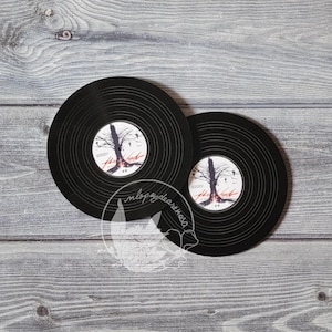 Puede incluir: Dos posavasos de vinilo negro con un diseño de árbol y pájaros. El texto "The Last" está impreso en los posavasos.