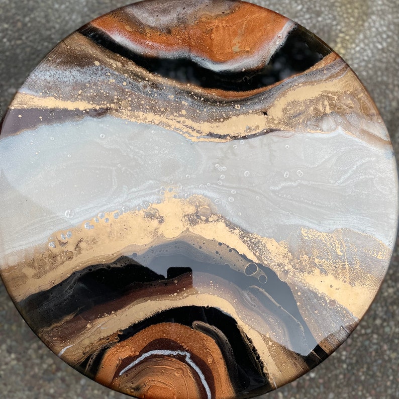 Puede incluir: Una pieza de arte redonda y abstracta con un acabado de resina. La obra de arte presenta un patr&oacute;n de remolino de colores negro, blanco, dorado y marr&oacute;n.