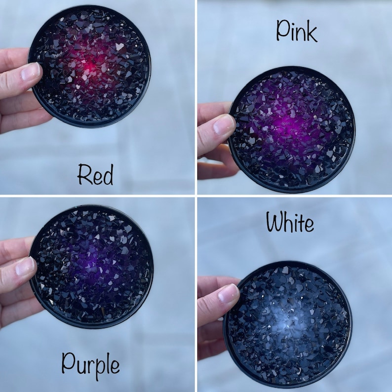 May include: Four round coasters with a black base and a center filled with black glass shards. The center of each coaster is filled with a different color: red, pink, purple, and white.