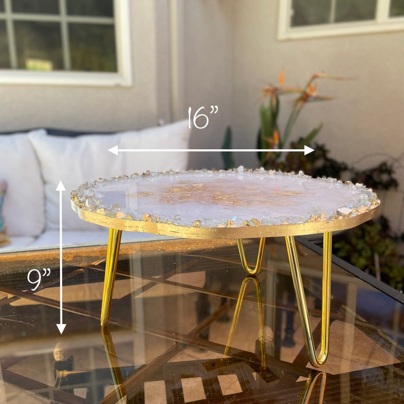 May include: A white and gold resin serving tray with a gold metal stand. The tray is 16 inches wide and 9 inches tall.