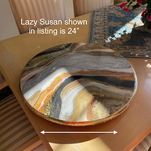 Puede incluir: Una Lazy Susan redonda de 61 cm de di&aacute;metro con un borde dorado y un dise&ntilde;o abstracto en espiral en resina negra, blanca, dorada y marr&oacute;n.