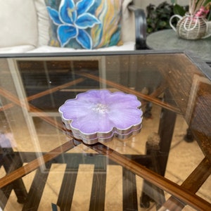 Op de afbeelding: Een paarse harsonderzetter met een bloemvormig ontwerp en een zilveren rand. De onderzetter ligt op een glazen tafel.