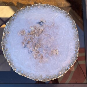 May include: White round resin coaster with a gold glitter design and a clear crystal edge.