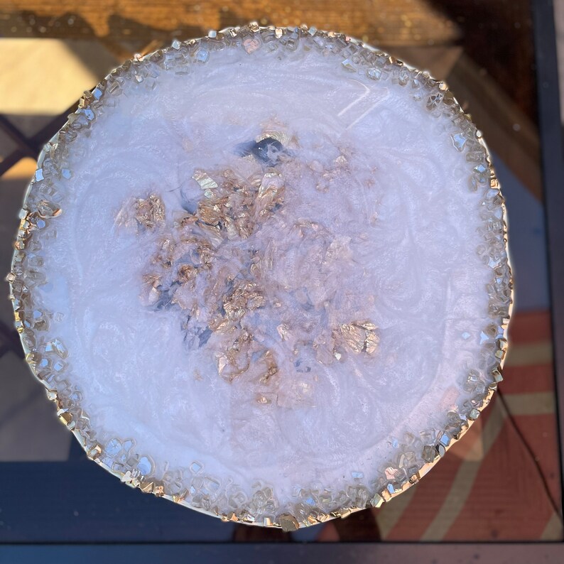 May include: White round resin coaster with a gold glitter design and a clear crystal edge.
