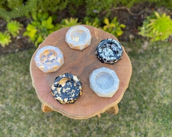 May include: Four decorative ashtrays with geometric shapes and gold accents. The ashtrays are made of resin and have a variety of colors, including white, black, and gray.