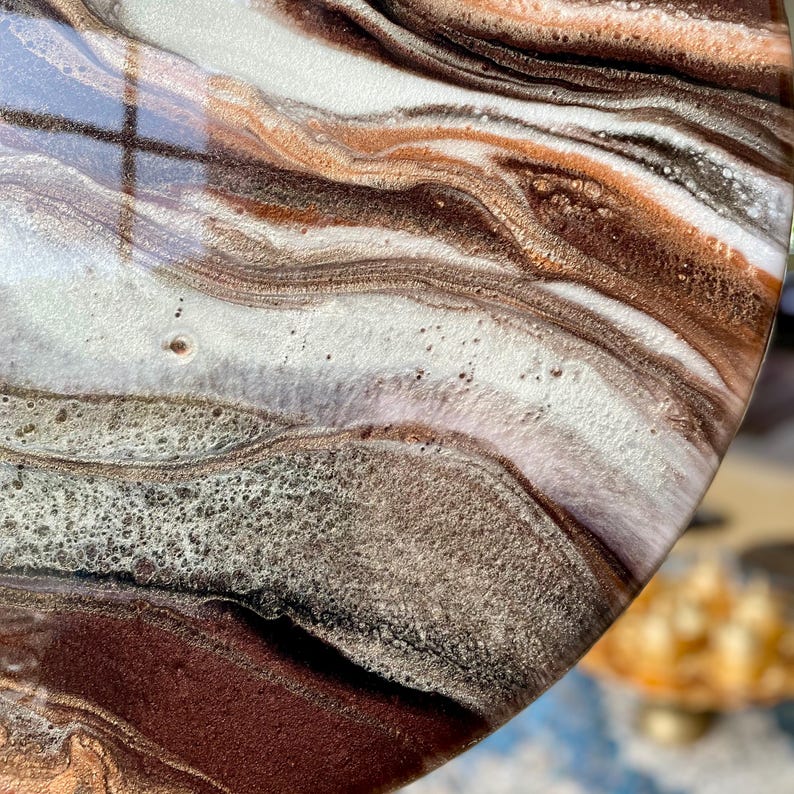 Op de afbeelding: Close-up van een rond, bruin, wit en gouden kunsthars kunstwerk met een draaiende, gemarmerde structuur. De hars is helder en glanzend, en de kleuren zijn levendig en rijk.