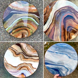 Op de afbeelding: Vier ronde harskunstwerken met abstracte, draaiende patronen in tinten van bruin, wit, blauw en goud. De harskunstwerken bevinden zich op een getextureerd oppervlak.