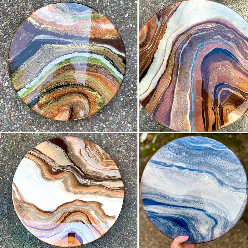 Op de afbeelding: Vier ronde harskunstwerken met abstracte, draaiende patronen in tinten van bruin, wit, blauw en goud. De harskunstwerken bevinden zich op een getextureerd oppervlak.