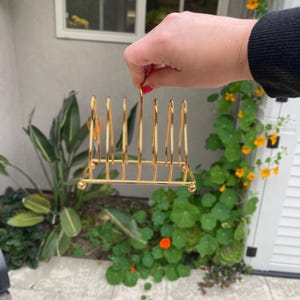 Puede incluir: Estante para platos de metal dorado con seis ranuras para sujetar los platos. El estante est&aacute; hecho de metal delgado y tiene un dise&ntilde;o simple.