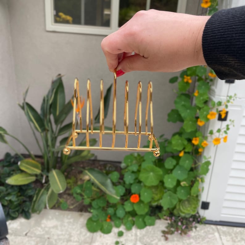 Puede incluir: Estante para platos de metal dorado con seis ranuras para sujetar los platos. El estante est&aacute; hecho de metal delgado y tiene un dise&ntilde;o simple.